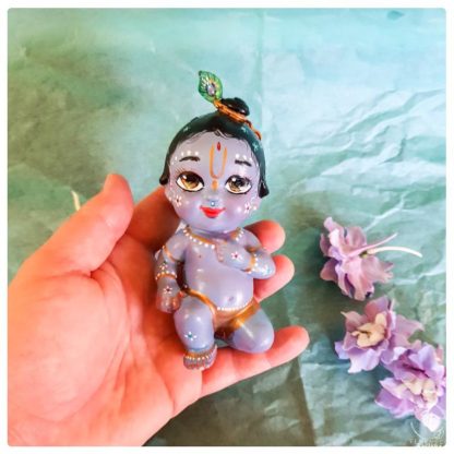 hand holding krishna doll figure blue skin blue background and lavender flowers