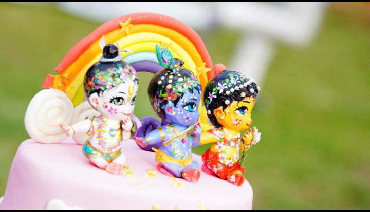 Rainbow background Radha doll krishna doll balaram doll on a cake pink and green background perfect devotee picture colorful and bright jewelled ornaments and peacock feathers