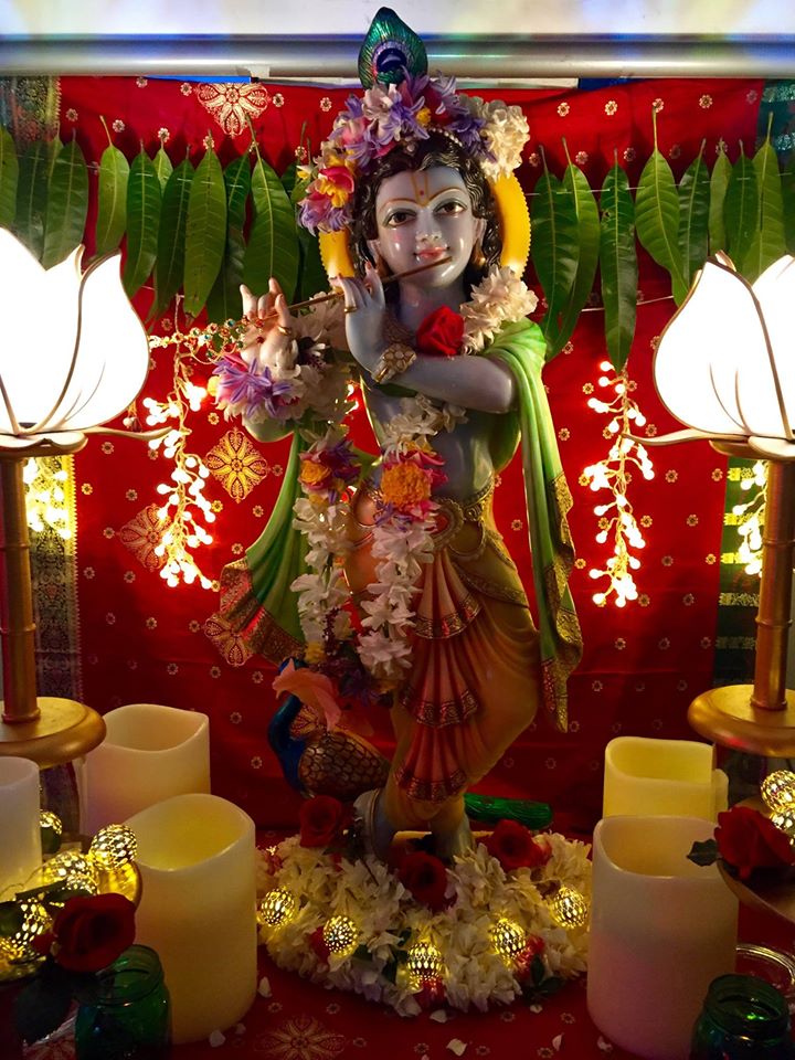 krishna marble statue on red background with mango leaf garland candles and white lotus lamps playing flute at krishna christmas celebration the mantra room gold coast
