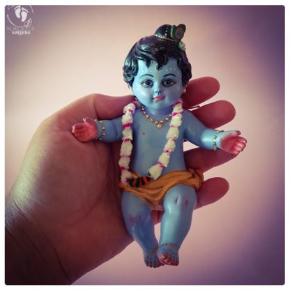 little baby krishna statue for janmastami perfect baby blue held in hand against pink background