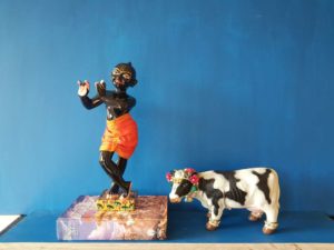 Krishnas cow stands next to him with flowers and golden anklets