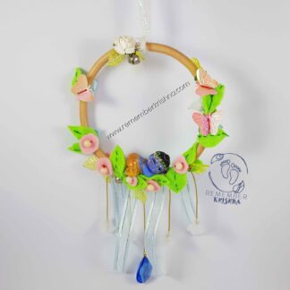 darling baby krsna doll nestled into leaves in a wooden hoop with a hanging blue jewel and sweet suspended flowers, pastel pink and leaves for wind chime which dangles like a dreamcatcher