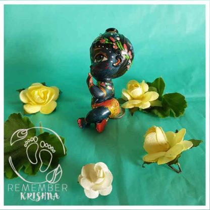 syamasundar Krishna_doll black skinn krsna doll for sale with lotus garland flower crown sitting on a turquoise background with yellow paper flowers around him for kids fun
