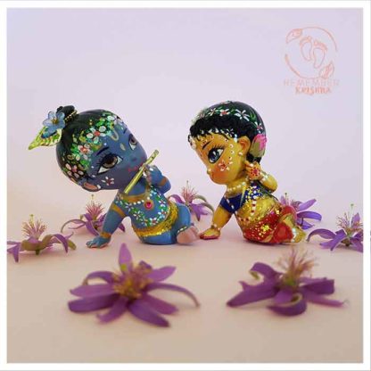 Radharani gazes lovingly at krsna radhe doll krishna doll pair for children with minature purple lotus flowers on pink background