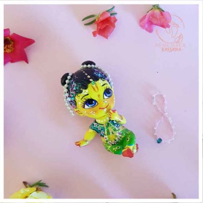 Lalita gopi doll on a pink background with a necklace of jewels and flowers dressed in peacock colored garments