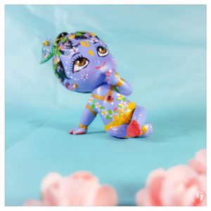 siting Krishna doll with flower garland and peacock feathers beautiful soft blue on blue turquoise background with pink flowers krsna doll