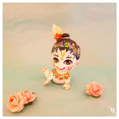 Crawling white skinned balaram doll with bun flower garlands and crawling on hands knees blue background with paper pink roses