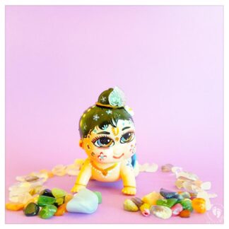 wind up balaram doll toy for kids vaishnava devotees white skin ostritch feather decorations and sitting on purple background with gemstones around.