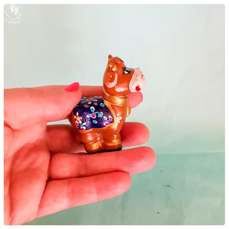 hand holding brown cow toy for krishna animal friends with blue blanket and pretty aqua backdrop