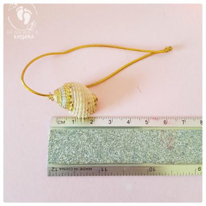 Gilded gold conchshell on a pink background and measured by glitter ruler on gold cord
