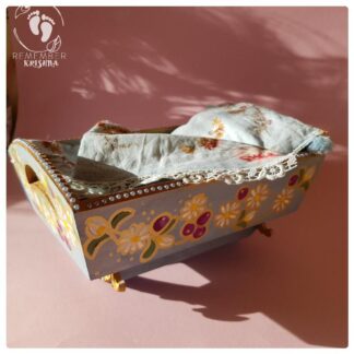rocking cradle for Krsna dolls painted blue with daisy and blueberry folk art style and blue flowery bedding wooden cradle on pink background
