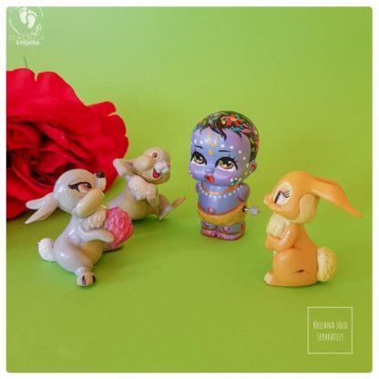 Krishna bunny rabbit friends toys on a green background with red fake roses and Krishna doll