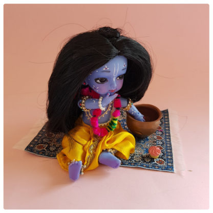 Oriental rug with Krsna doll sitting on rug having a picnic cupcake