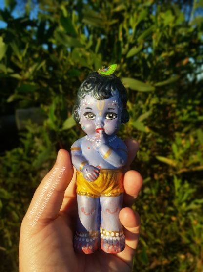 baby krishna doll soft blue color held in hand against a forest background