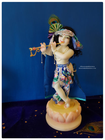 Krishna deity 12 inch on lotus base sri Hari wearing a white silken peacock themed dhoti with a blue shawl, a turban layered with multiple peacock fans and photographed against a deep blue background rememberkrishna deity murti of krishna for sale