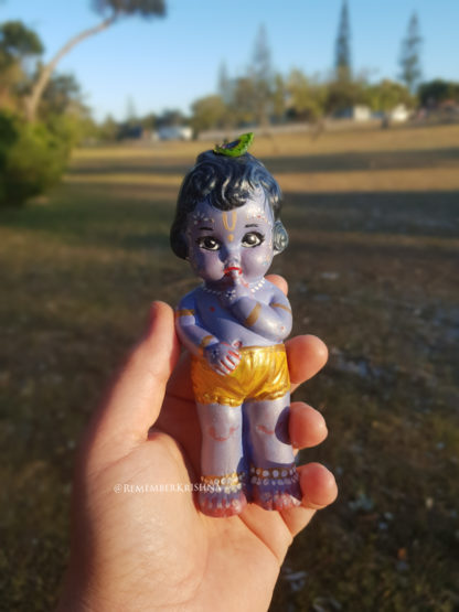 baby krishna standing tall with hand to mouth looking worried, held in hand