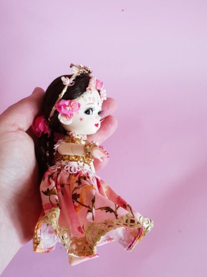 Shri Radha doll with gorgeous braids and flower crown poseable radha doll held in hand side view against pink background