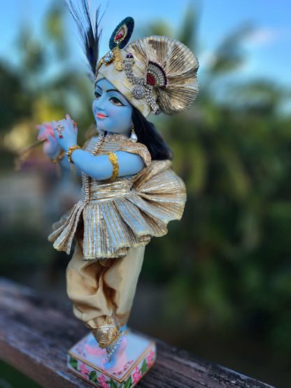 Mohana krishna deity blue deity of Krishna dressed in yellow garments with a red turban and peacock feather in his hair and playing the flute golden bhagavad geeta armour outfit