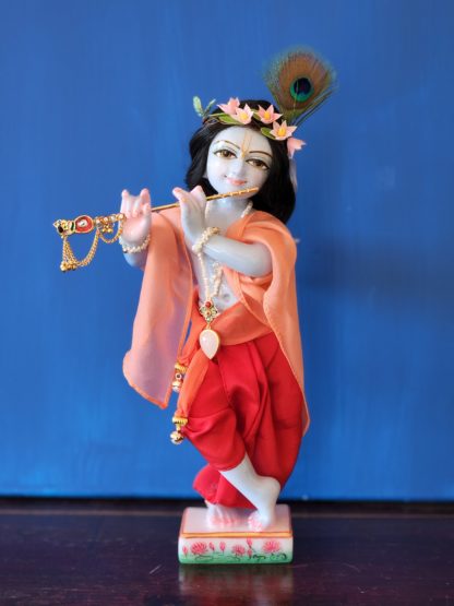 krishna deity 12 inch white marble blue colorwash hue skin dressed in red dhoti murti in three fold bending post with flute peach shawl hair and peacock feather on blue background