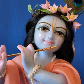 krishna deity 12 inch white marble blue colorwash hue skin dressed in red dhoti murti in three fold bending post with flute peach shawl hair and peacock feather on blue background
