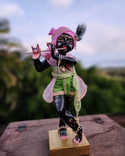 govind krishna deity 12 inch black marble deity with gold base dressed in elaborate shrngar against forest background krishna deity holds flute and wears peacok feather