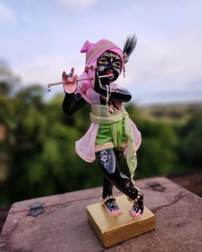 govind krishna deity 12 inch black marble deity with gold base dressed in elaborate shrngar against forest background krishna deity holds flute and wears peacok feather