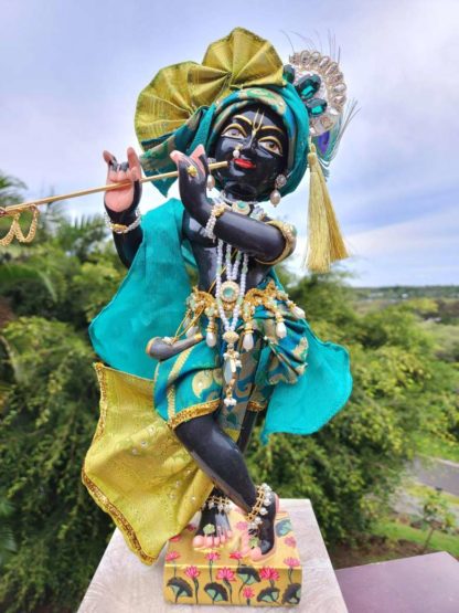 deity black marble form of lord krishna murti radha kanta wearing peacock coloured garments and holding a flute