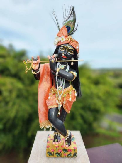 deity black marble form of lord krishna murti radha kanta wearing apricot coloured garments and holding a flute