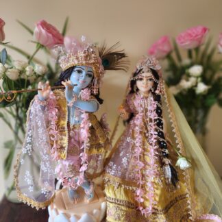 radha krishna marble deities on a carved lotus base dressed in yellow and pink shringar