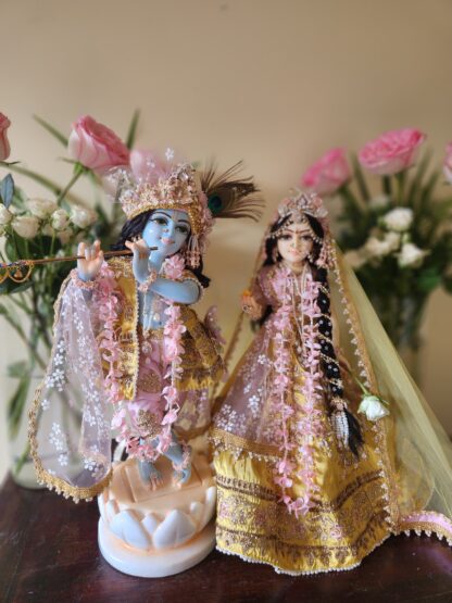 radha krishna marble deities on a carved lotus base dressed in yellow and pink shringar