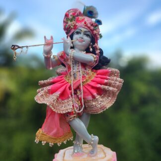 deity of krishna dressed in elaborate pink strawberry inspired shringar playing flute and standing on lotus base