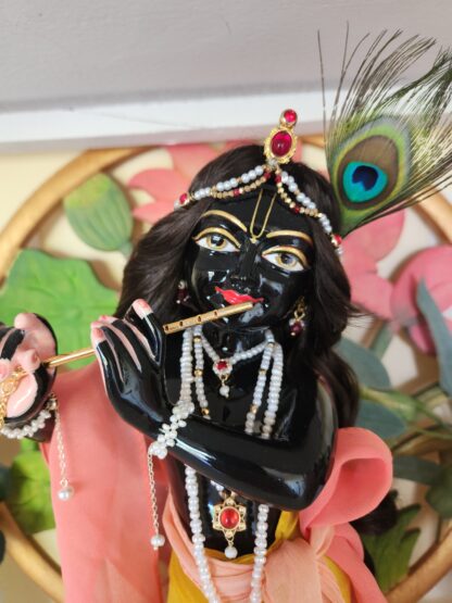 black marble deity of krishna with pearl adornments and yellow and pink outfit close up view of face