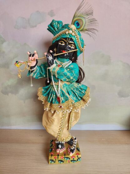 Black marble deity of Krishna wearing a peacock feather for comparison next to the form of the lord dressed in gold and green shringar