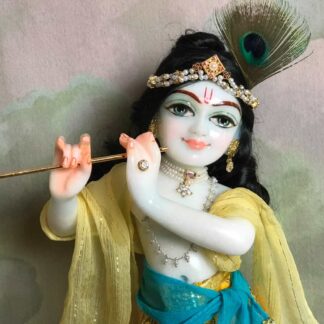 Quality white marble krishna deity hand carved Kamal Nayana weearing soft pink outfit with delicate pink hands in a pink turban and a peacock feather with delicate pearl and gold jewelery 12inch tall deity of Krishna shown holding flute. deity pictured in slight side profile focus on face and peacock feather with jeweled crown