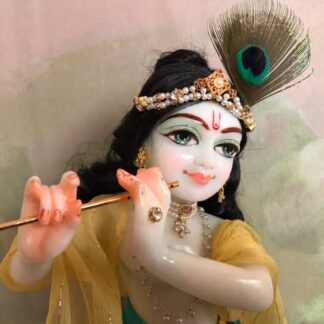 Quality white marble krishna deity hand carved Kamal Nayana weearing soft pink outfit with delicate pink hands in a pink turban and a peacock feather with delicate pearl and gold jewelery 12inch tall deity of Krishna shown holding flute. deity pictured in slight side profile focus on face and peacock feather with jeweled crown