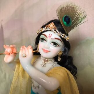 Quality white marble krishna deity hand carved Kamal Nayana weearing soft pink outfit with delicate pink hands in a pink turban and a peacock feather with delicate pearl and gold jewelery 12inch tall deity of Krishna shown holding flute. deity pictured in slight side profile focus on face and peacock feather with jeweled crown