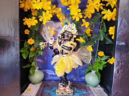 showing a soft, open rose being offered at the feet of a thirteen-inch black marble Krishna deity (Sarveshwara Krishna). The camera then pans up to reveal His full bumblebee outfit: a velvet silk dhoti, a gauzy overskirt with pearls and flowers, a yellow-ruffled striped vest with diamonds, a sparkling mukut with flowers, and a shimmering gauzy shawl.