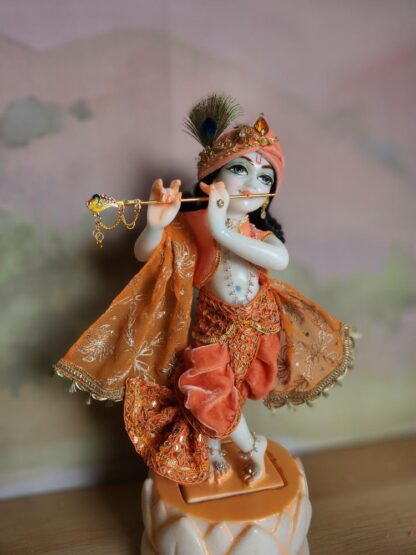 BalaGopal deity Quality white marble krishna deity hand carved Kamal Nayana weearing soft pink outfit with delicate pink hands in a pink turban and a peacock feather with delicate pearl and gold jewelery 12inch tall deity of Krishna shown holding flute. deity pictured in slight side profile focus on face and peacock feather with apricot and peach gorgeous dhoti