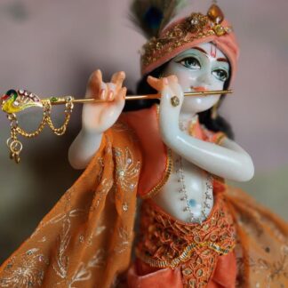 BalaGopal deity Quality white marble krishna deity hand carved Kamal Nayana weearing soft pink outfit with delicate pink hands in a pink turban and a peacock feather with delicate pearl and gold jewelery 12inch tall deity of Krishna shown holding flute. deity pictured in slight side profile focus on face and peacock feather with apricot and peach gorgeous dhoti