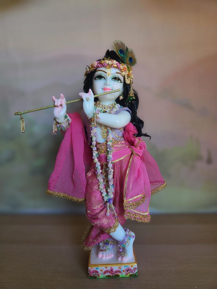 A marble Gopal Krishna deity wearing a pink silk dhoti with gold floral patterns, a pink shawl, and a violet lace vest.
