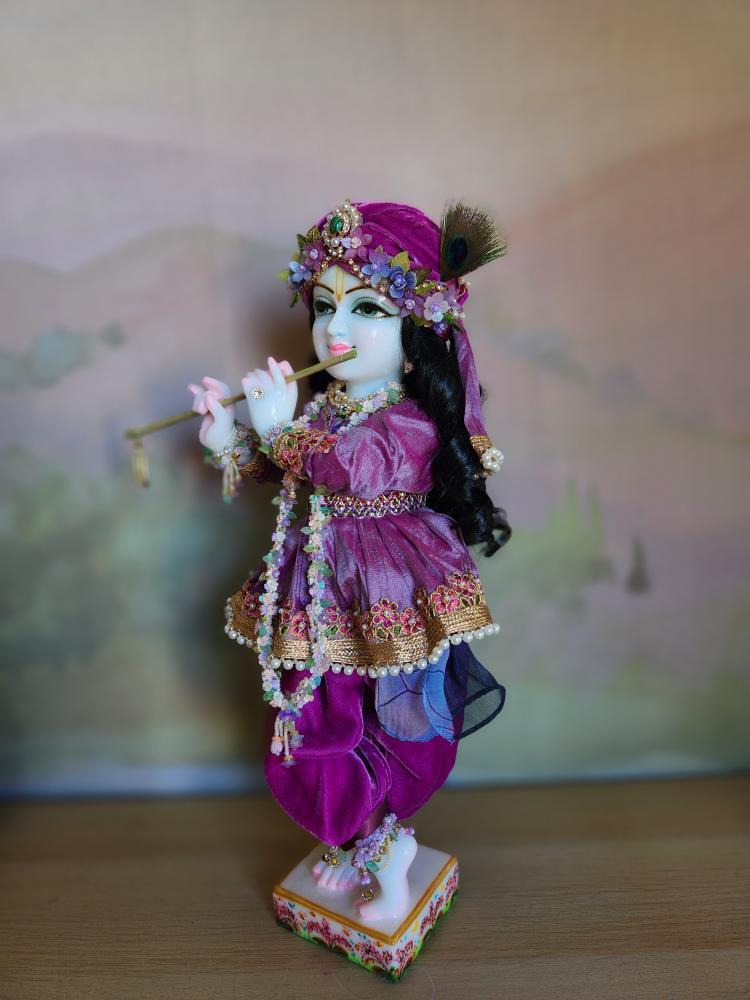 A marble Gopal Krishna deity wearing an ornate purple velvet outfit with a jeweled turban and a peacock feather.