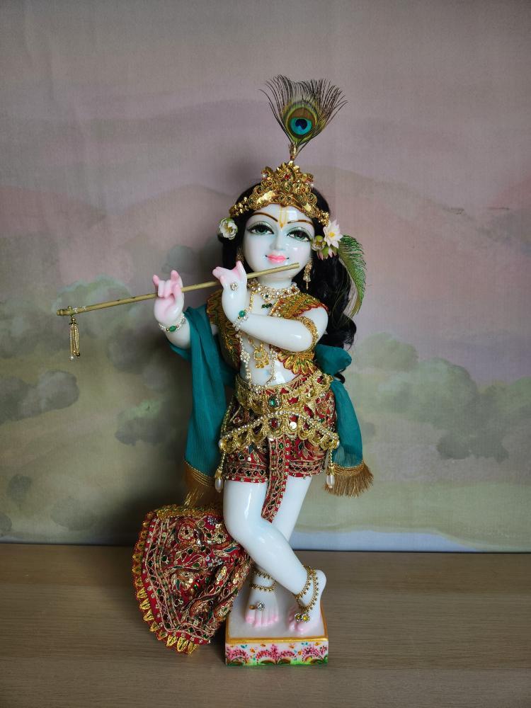 A marble Gopal Krishna deity in a scarlet silk cowherd boy outfit with a gold vest and a detachable jeweled pleated sash.