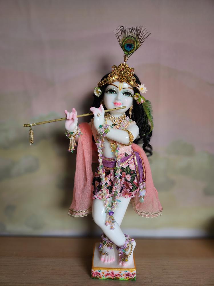 A marble Gopal Krishna deity in a playful short dhoti with a purple and pink daisy print, a lavender sash, and a pink shawl.