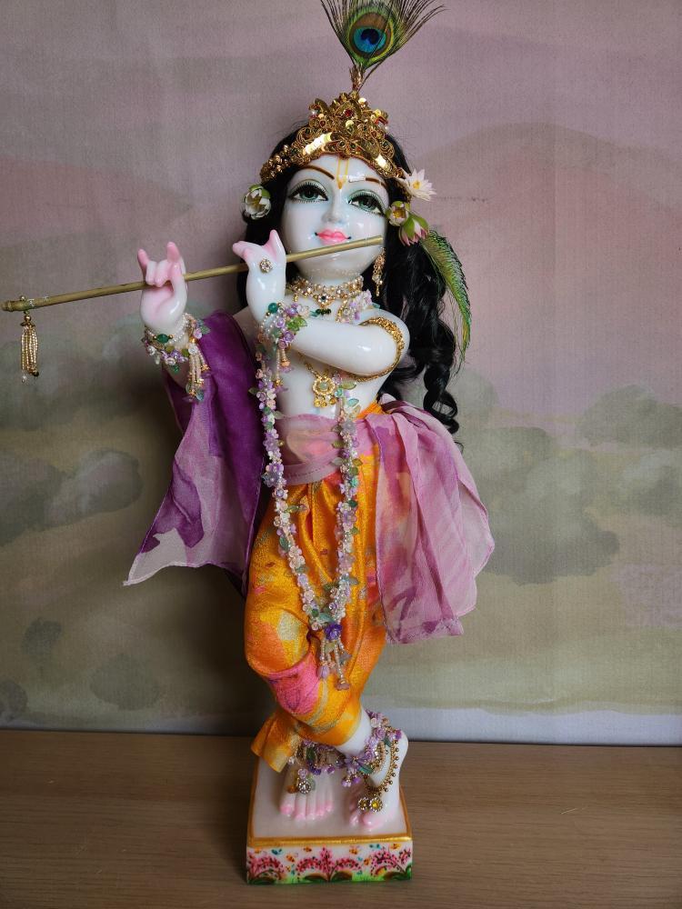 A marble Gopal Krishna deity wearing a flowing yellow dhoti with a wispy violet and pink sash and shawl.