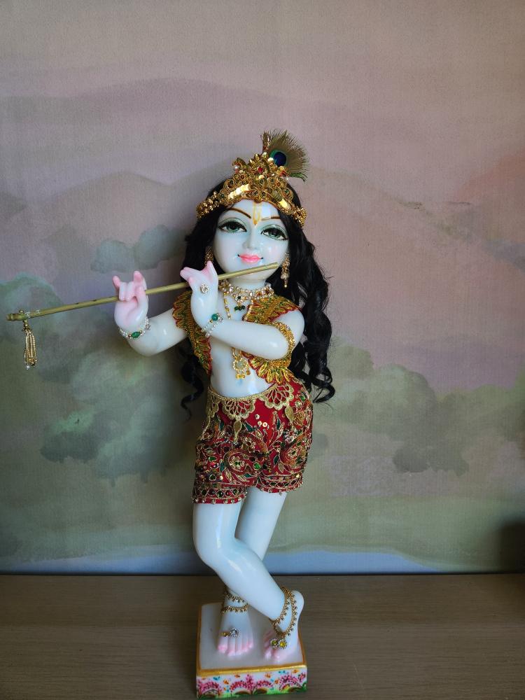 A marble Gopal Krishna deity in a scarlet silk cowherd boy outfit with a gold vest and a detachable jeweled pleated sash.