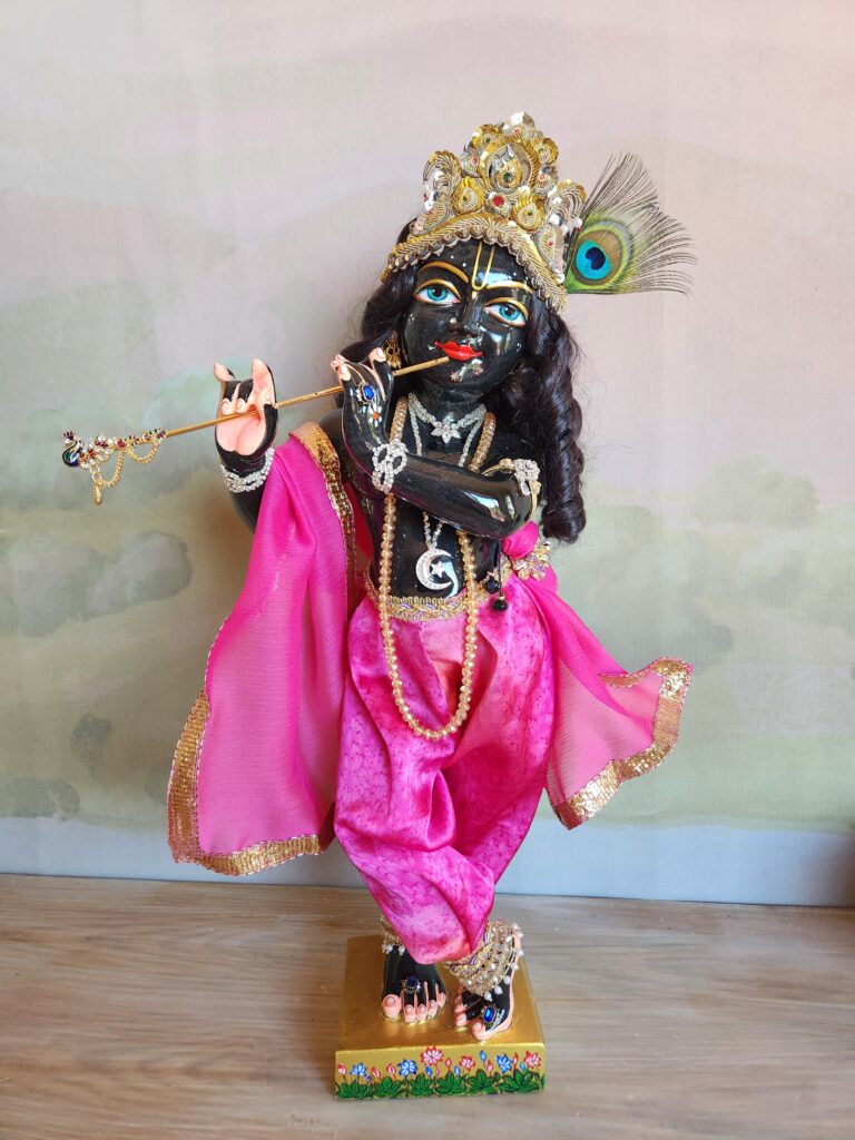 Syamasundar Krishna dressed in pink shawl and pink silk pants against a background of dawn
