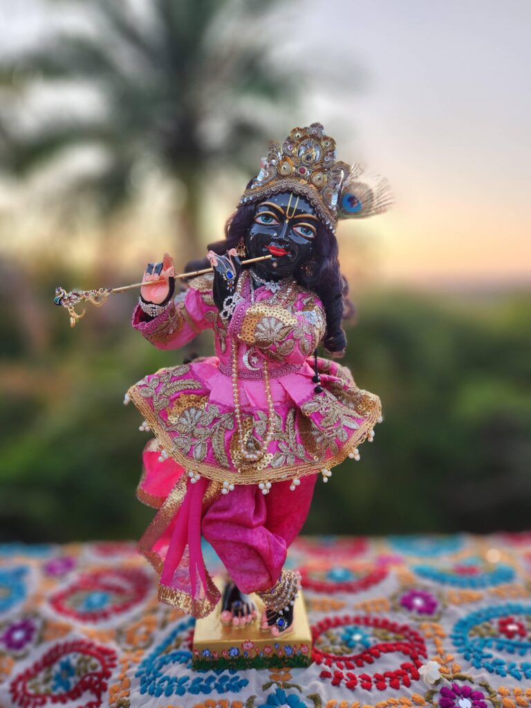 Syamasundar Krishna dressed in pink jacket and pink silk pants against a background of dawn