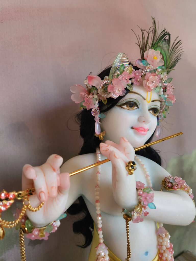 Krishna deity wearing flowery jewellery crown in pink