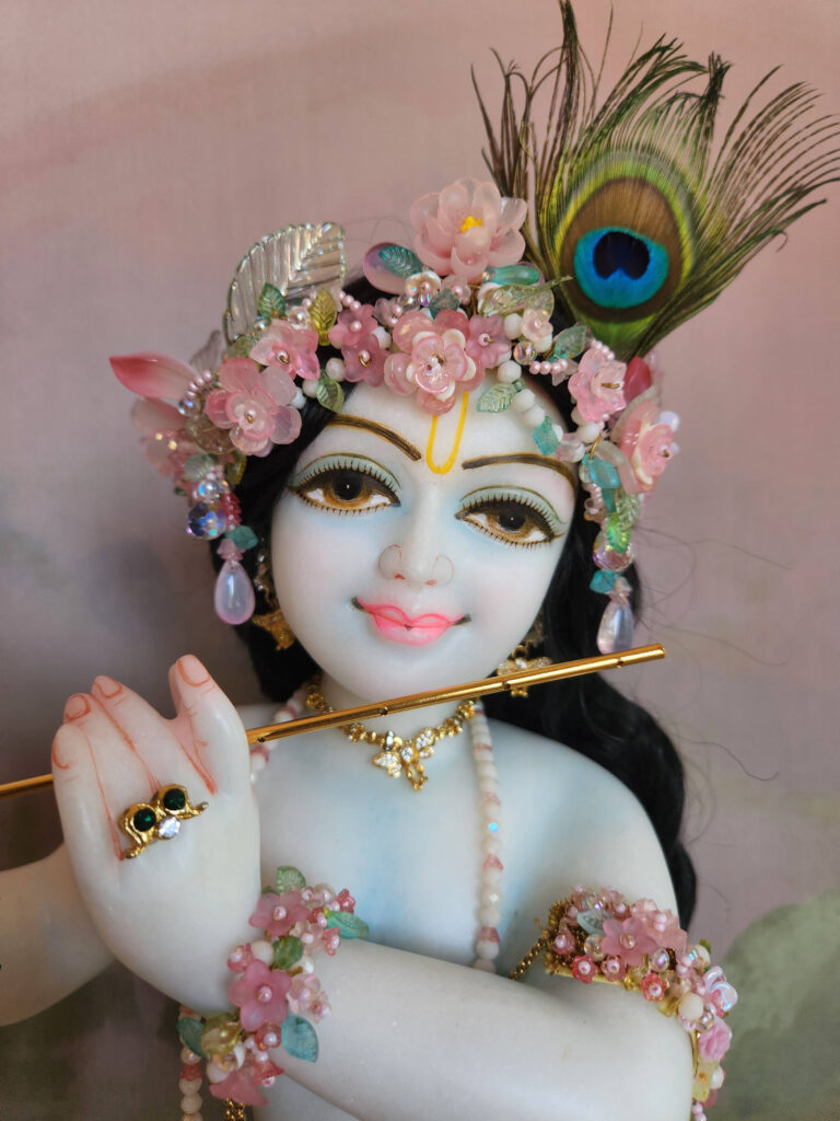 Krishna deity wearing flowery jewellery crown in pink