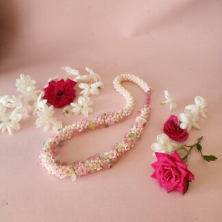 Jewelery for deity Krishna beaded garland flower mala necklace made with crystals, beads and leaves photographed with fresh jasmine and roses on a pink background